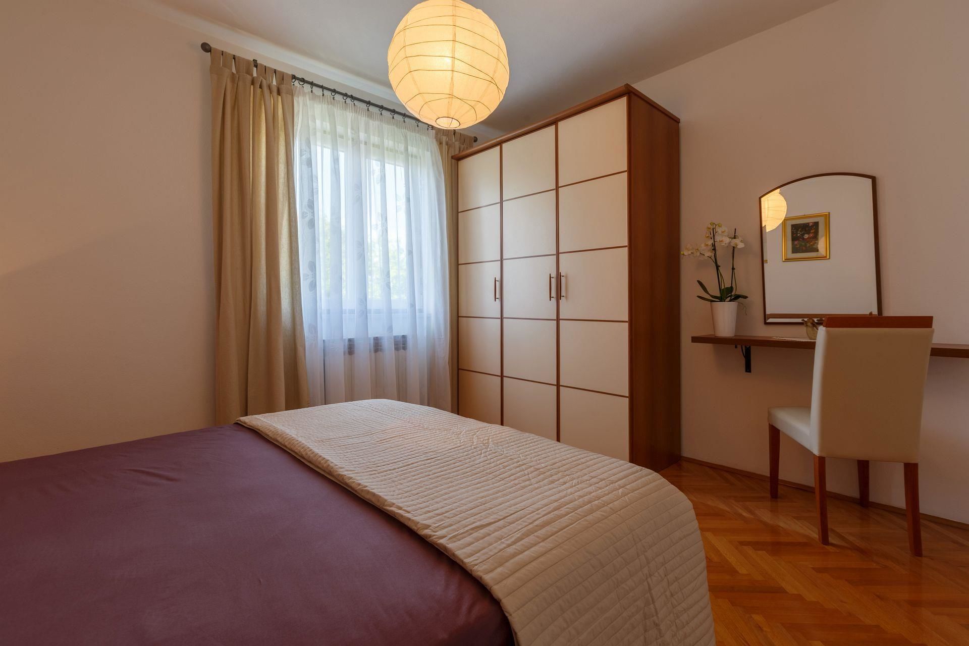 Een slaapkamer met een bed, een bureau met stoel, een garderobe en een hanglamp.