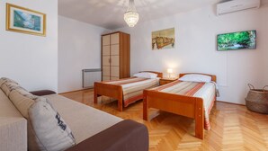 Una stanza con due letti di legno, un divano, un lampadario, un termosifone, un armadio, una televisione e un quadro appeso al muro.