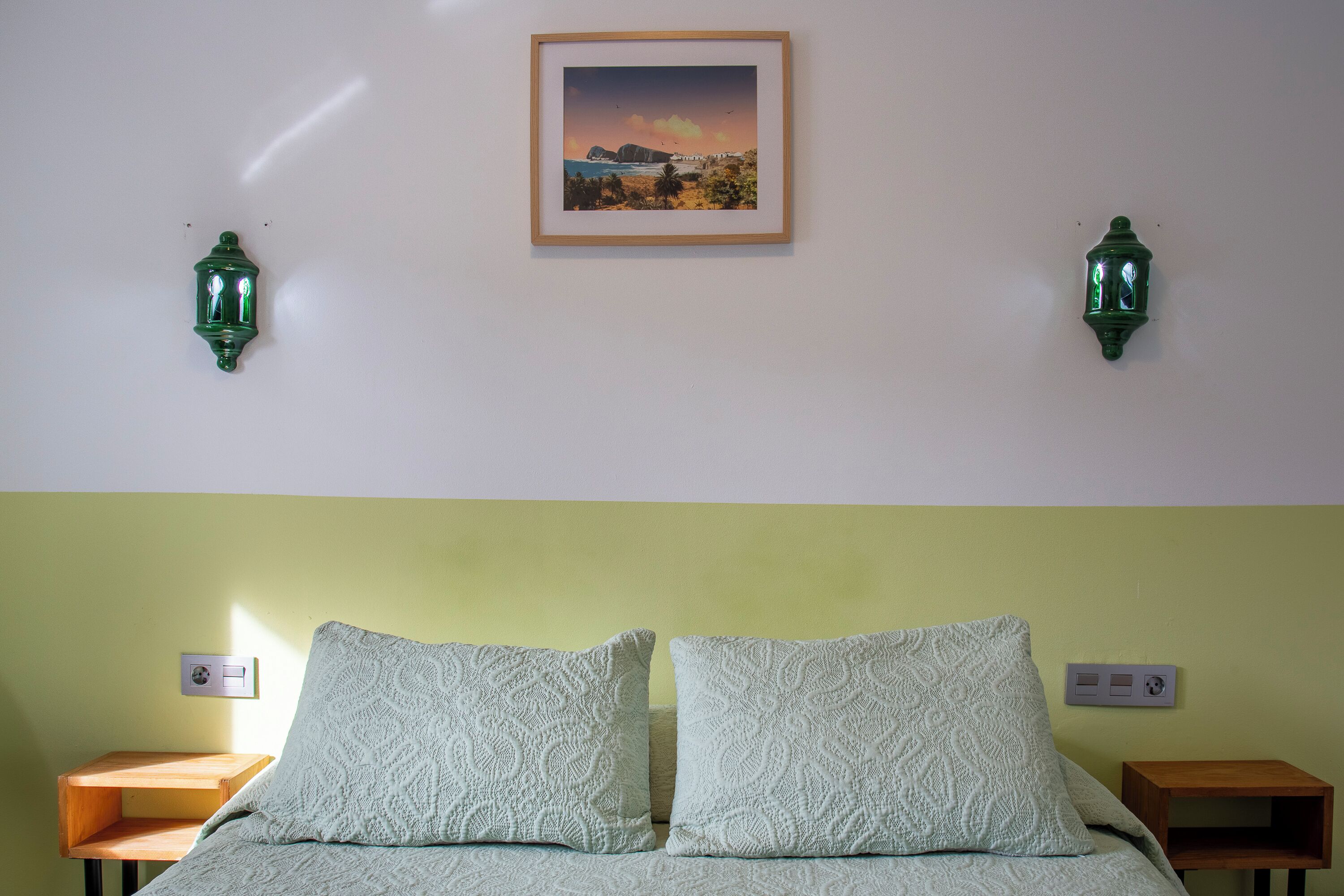 Ein Schlafzimmer mit einem Bett, zwei Nachttischen, einem gerahmten Bild an der Wand und zwei Wandlampen.