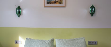 Un dormitorio con una cama, dos mesitas de noche, un cuadro enmarcado en la pared y dos lámparas de pared.
