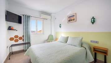 Un dormitorio con cama, televisión, ventana, silla y una mesita.
