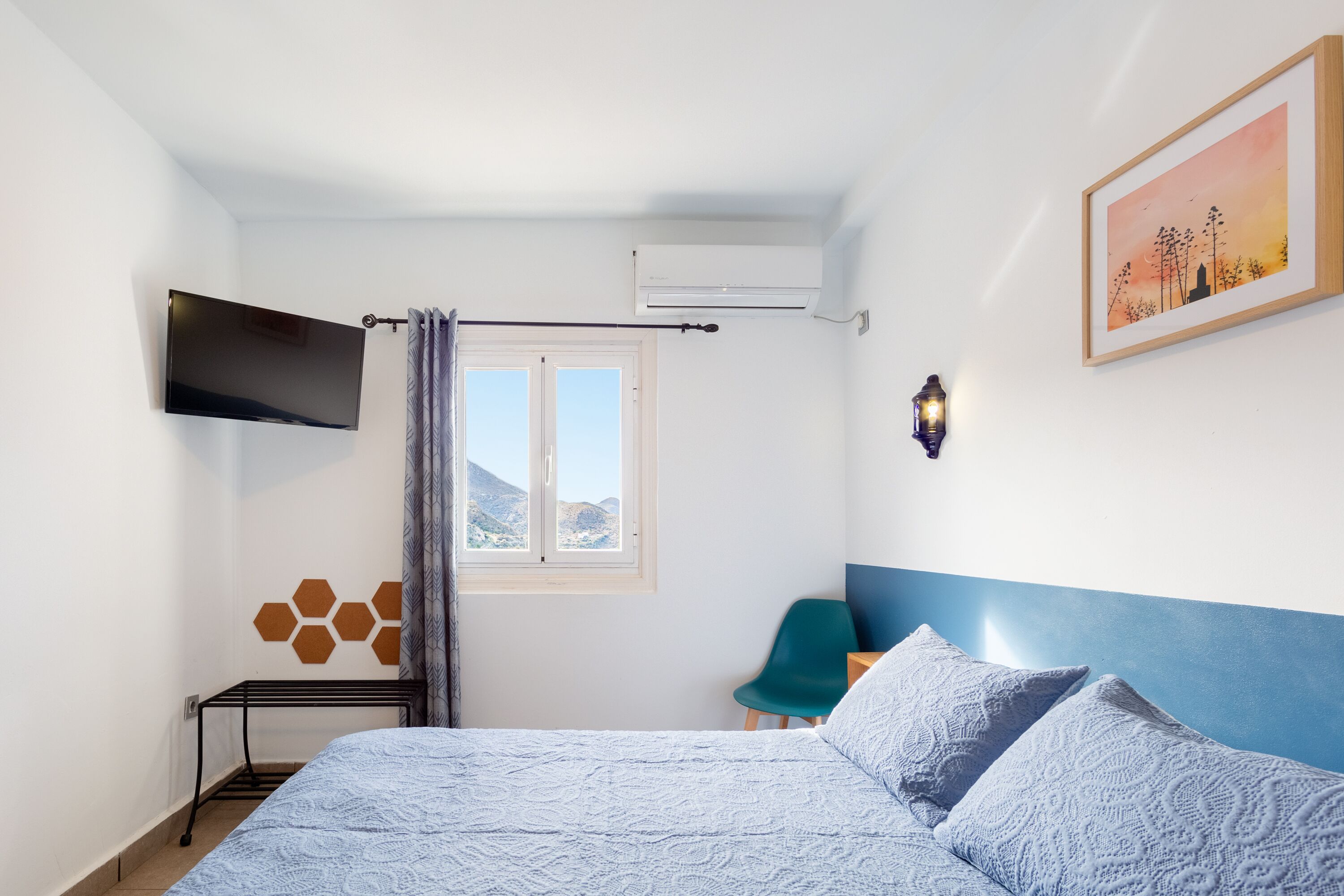 A bedroom with a bed, a TV, a window, a chair, and a wall-mounted air conditioner.