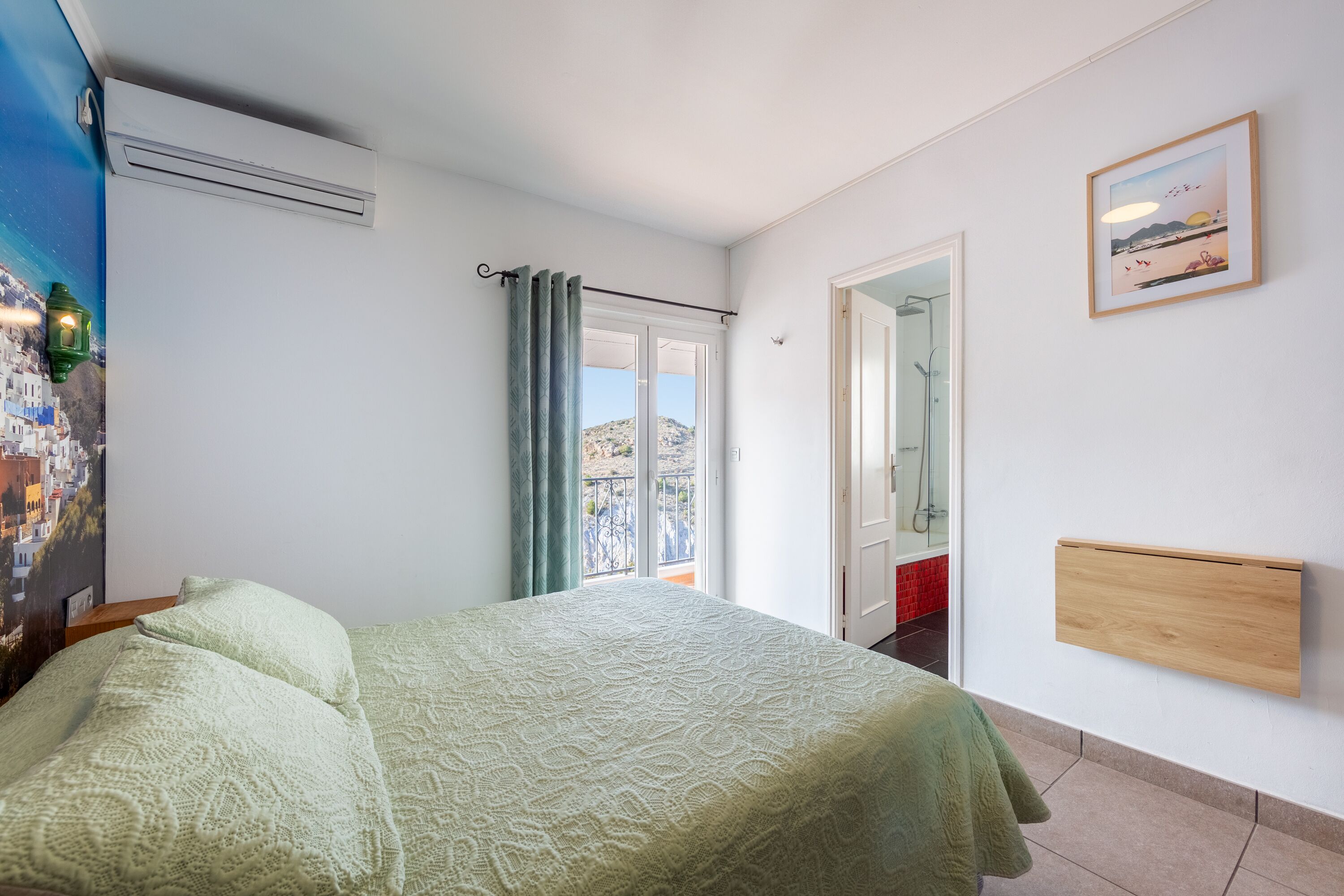 A bedroom with a bed, a window with curtains, a door, a wall-mounted shelf, and a painting.
