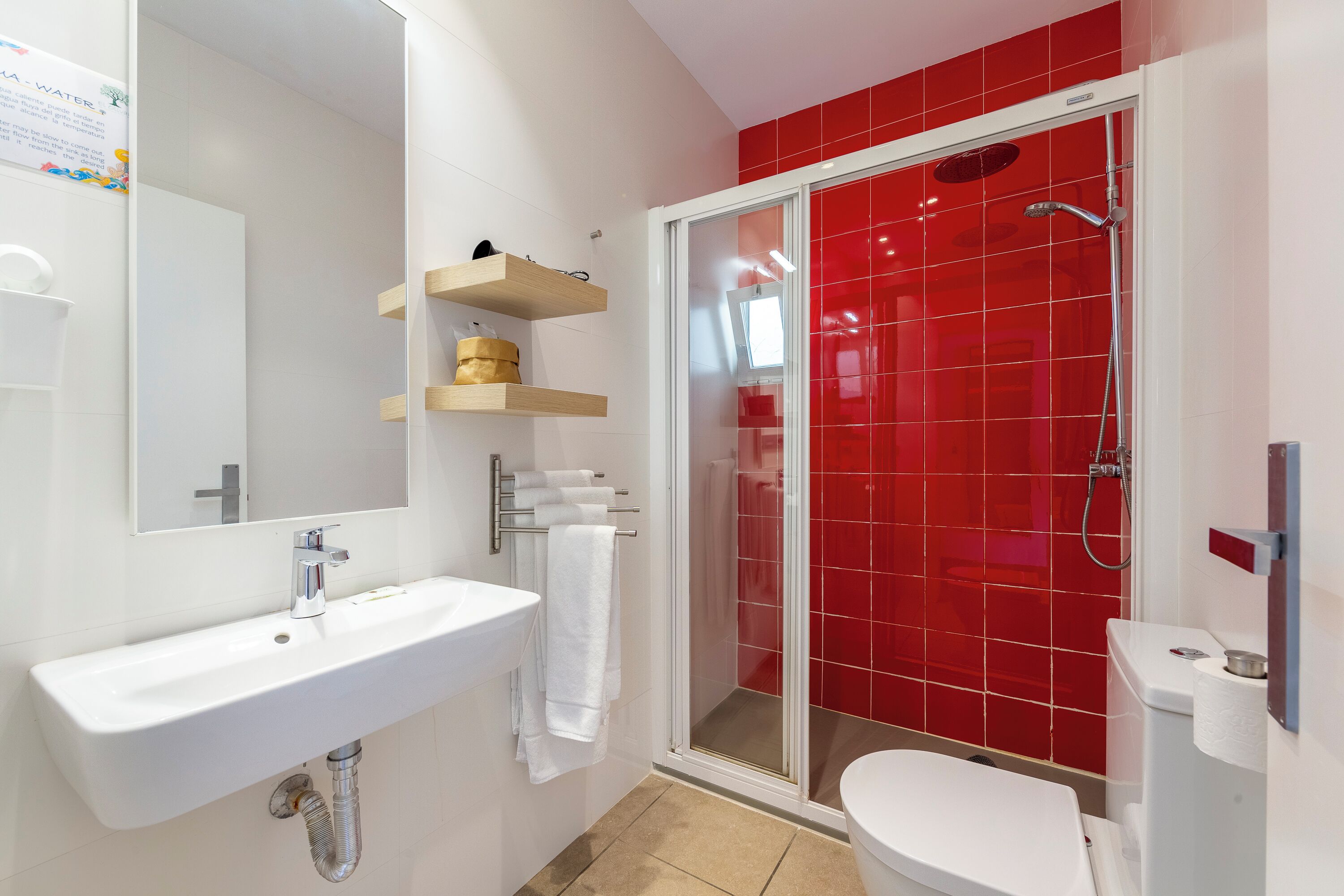 Une salle de bain moderne avec un lavabo blanc, une douche en verre et des murs recouverts de carreaux rouges.