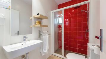 Un baño moderno con un lavamanos blanco, una ducha con cerramiento de vidrio y paredes con azulejos rojos.