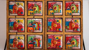 A wooden frame with twelve colorful tiles, each depicting a stylized house.