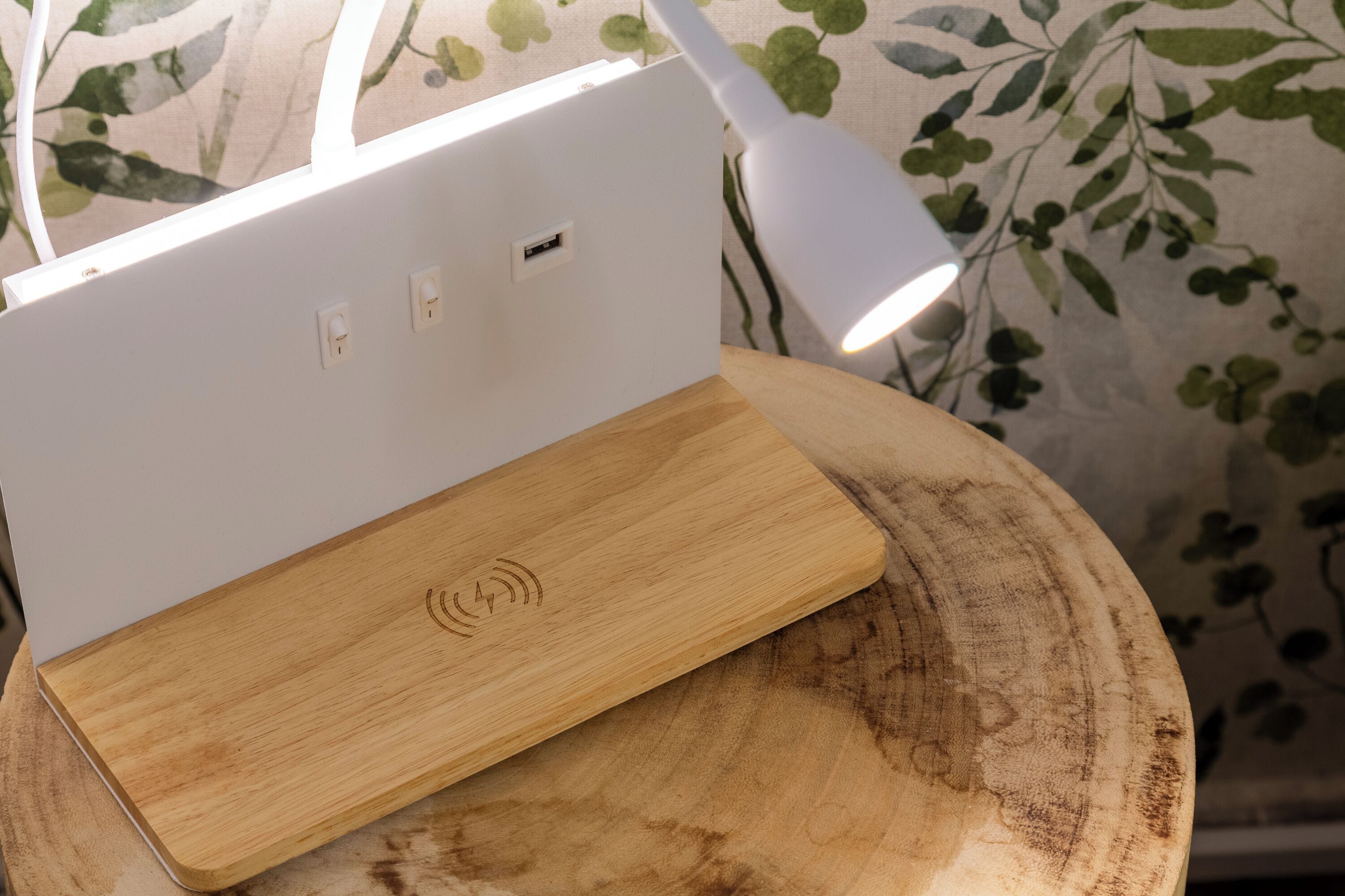 Un portátil blanco sobre un atril de madera con una lámpara blanca a su lado.