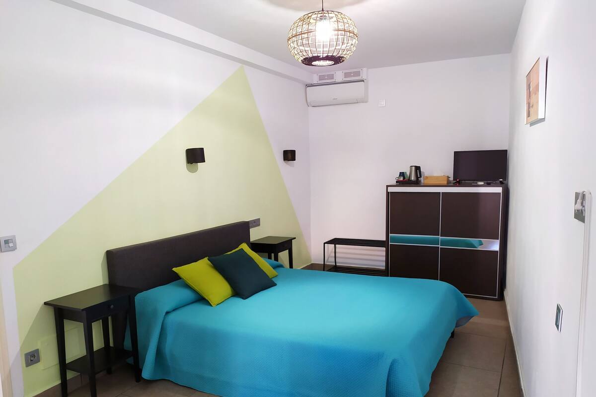 Un dormitorio con cama, mesitas de noche, televisor, cafetera y armario.