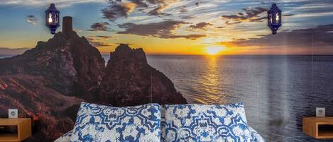 A bedroom with a bed, two nightstands, and a wall mural of a sunset over the ocean.