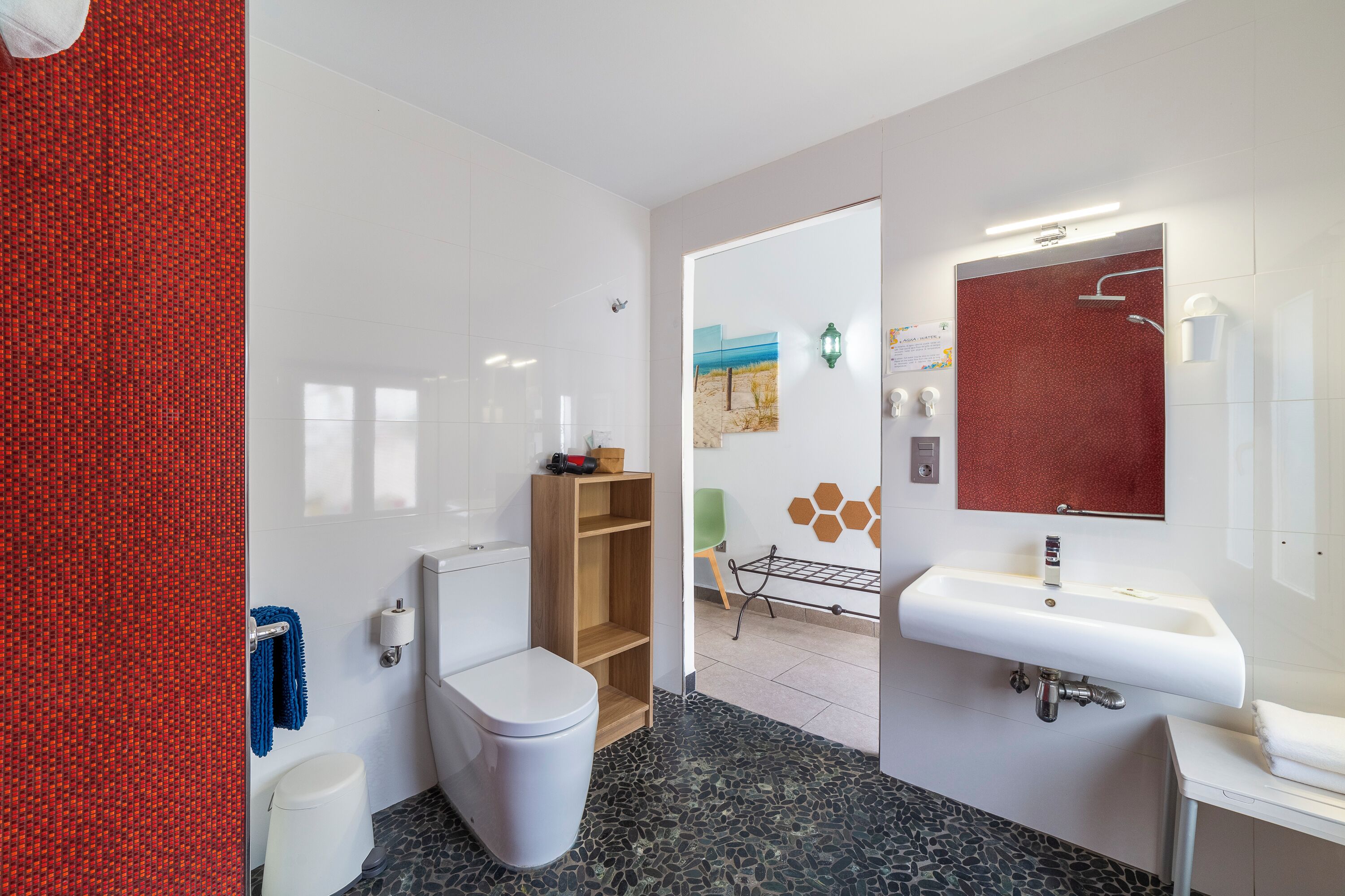 A modern bathroom with a white toilet, a wooden shelf, a white sink, and a shower area.