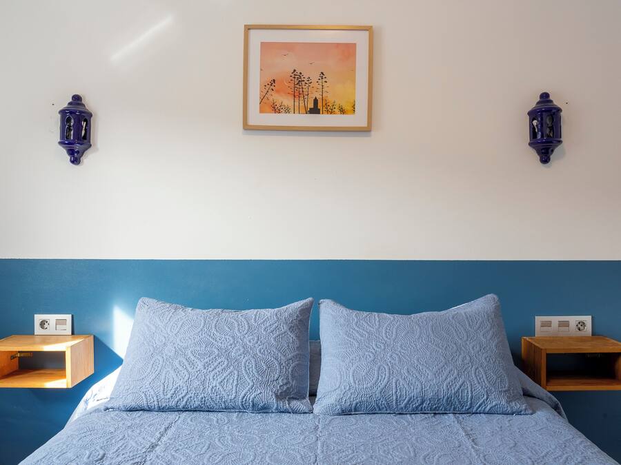 A bedroom with a bed, two wall-mounted nightstands, and a framed picture on the wall.