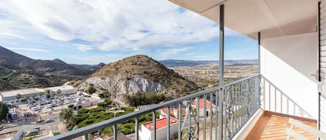 A balcony with a view of a mountainous landscape, a parking lot, and buildings with red roofs.