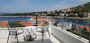 A balcony with a table and chairs overlooking a coastal town with red-roofed buildings and a body of water. - Apartments MIA Bilo 887 (Primosten)