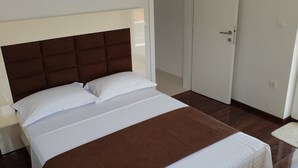 A neatly made bed with white linens and a brown headboard in a room with wooden flooring and white walls. - Apartments MIA Bilo 887 (Primosten)