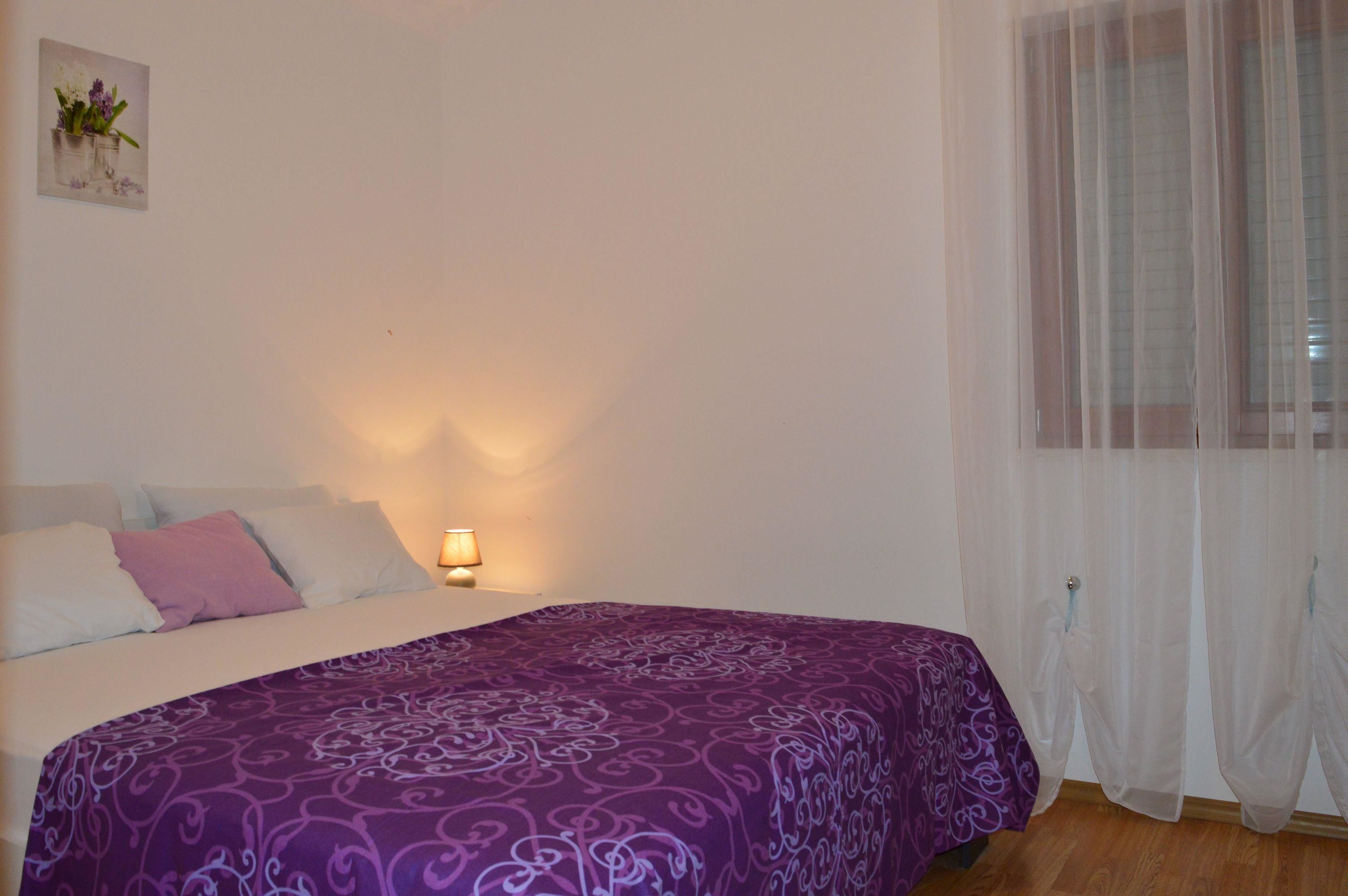 A bedroom with a bed, a bedside lamp, and a window with sheer curtains.