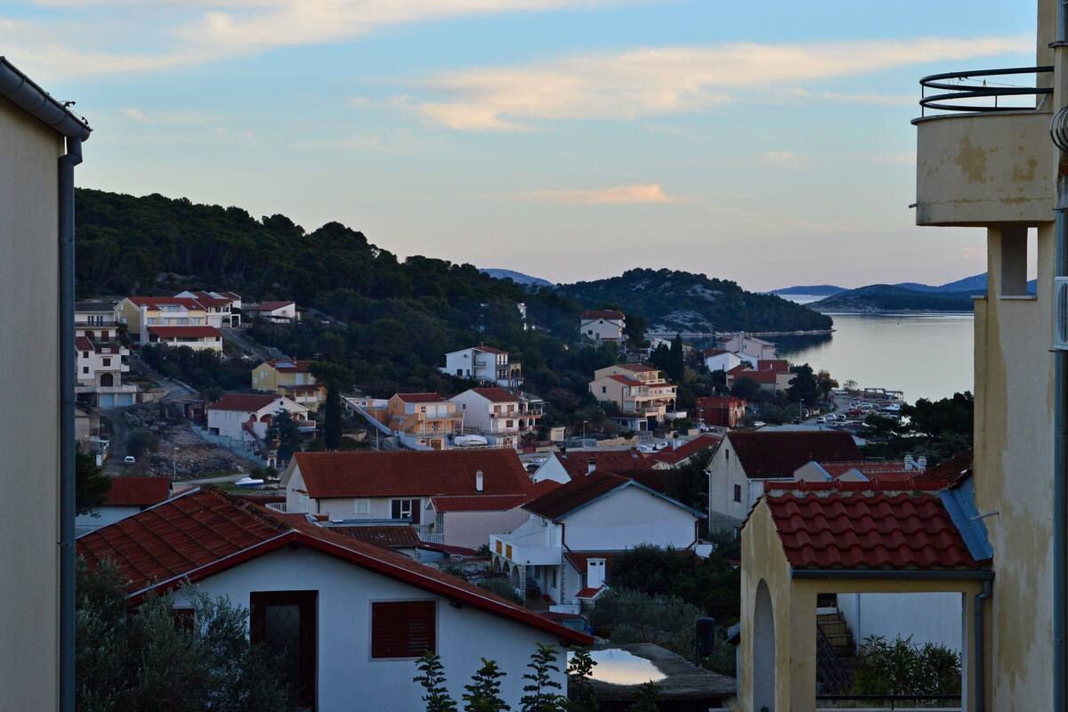 A coastal town with buildings, a water body, and hills in the background.
