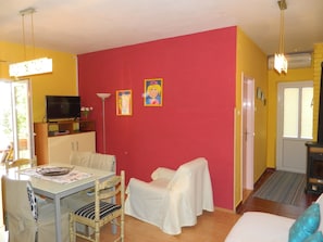 Una habitación con pared roja, una mesa blanca con sillas, un televisor y una chimenea.