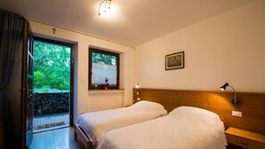 A room with two beds, a window with a view of greenery, a wooden headboard, a bedside lamp, and a cross on the wall. - Fattoria Carsica Bajta (Sgonico)
