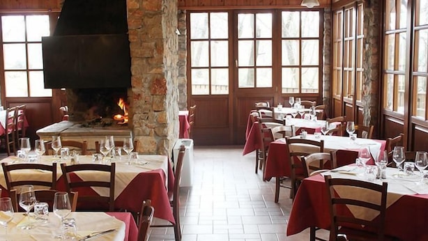 A restaurant with multiple tables, each set with wine glasses and plates, and a large stone fireplace with a fire. - Fattoria Carsica Bajta (Sgonico)