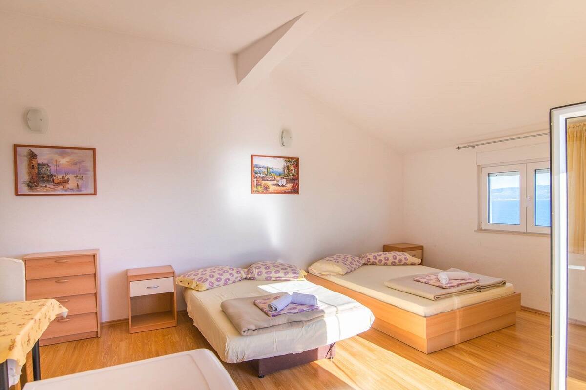 A bedroom with a bed, a bedside table, a chair, and two paintings on the wall.