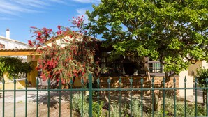A traditional house with a brick facade, a wooden balcony, and a green metal fence in the foreground. - Maria's Countryside House (Corfu)