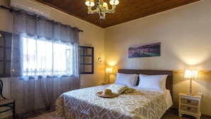 A neatly arranged bedroom with a bed, two bedside tables with lamps, a chair, and a window with curtains. - Maria's Countryside House (Corfu)