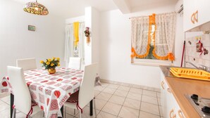 A dining area with a table set for four, a hanging light fixture, and a window with curtains. - Apartments Villa Dane (Podstrana)
