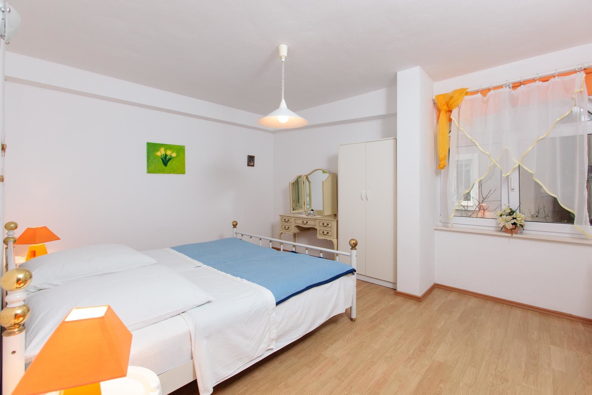 Ein Schlafzimmer mit Bett, Nachttischlampen, einem Kleiderschrank, einem Spiegel und einem Fenster mit Vorhängen.