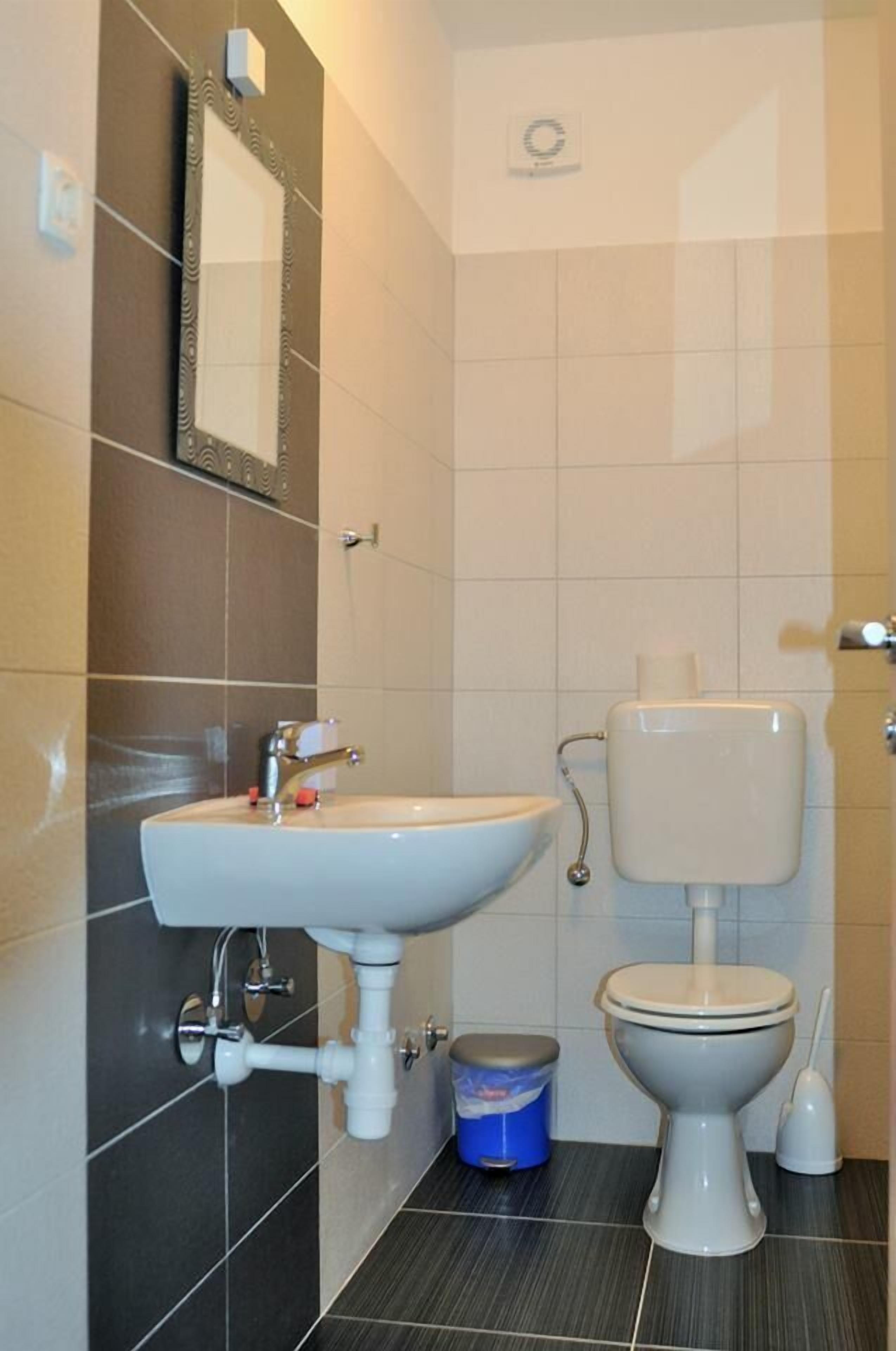 A bathroom with a white sink, a toilet, and a blue trash bin.