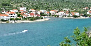 A coastal village with houses along the shoreline, a boat on the water, and a hilly landscape in the background.