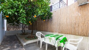 A patio with a table and chairs, a tree with oranges, and a bamboo wall. - Apartments Cagalj (Trogir)