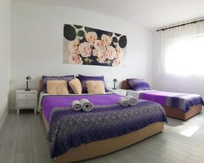 A bedroom with two beds, a nightstand with a lamp, a wall-mounted painting of roses, and a window with curtains. - Apartments Cagalj (Trogir)