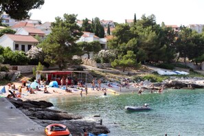 A beach with people sunbathing and swimming, a small boat, and a red structure. - Apartments Sanader (Okrug)