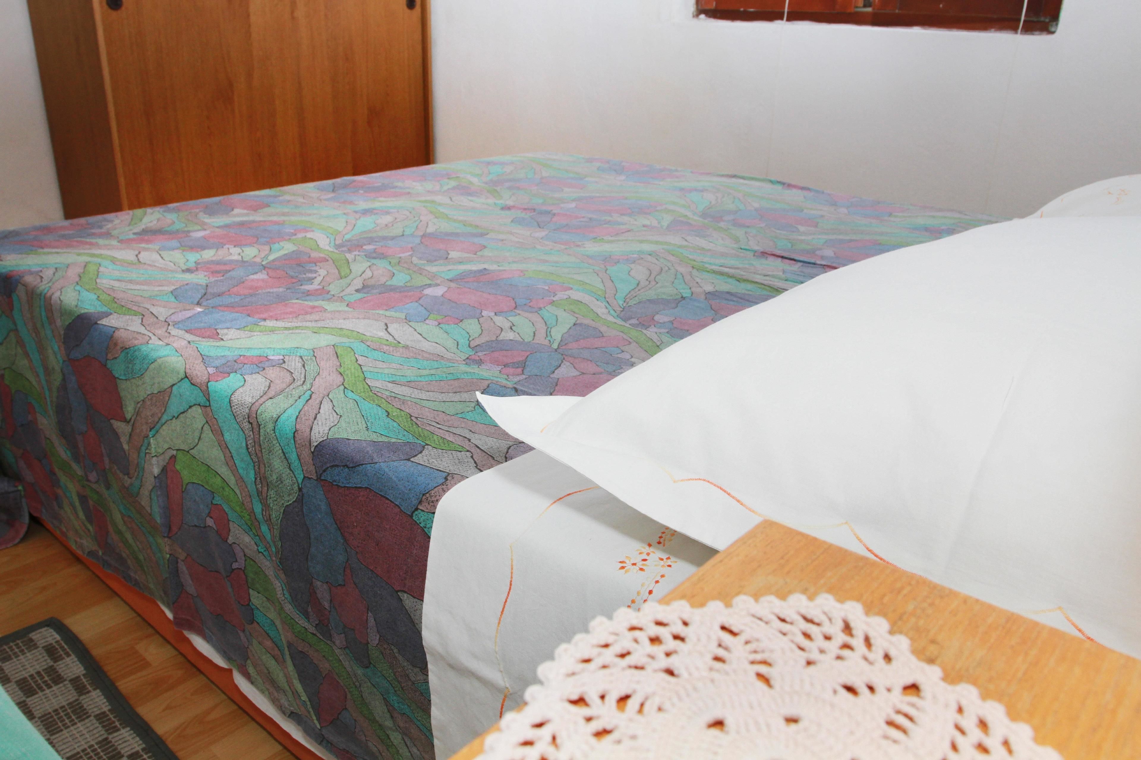 A bed with a colorful patterned bedspread and a white pillow.