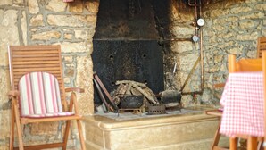 Ein Kamin aus Stein mit Holzscheiten, ein hölzerner Stuhl und ein Tisch mit karierter Tischdecke.