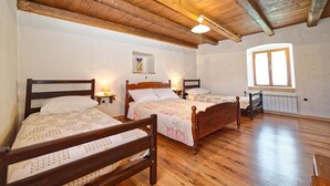 Ein Zimmer mit drei Holzbett, Holzboden, Holzbalkendecke, einem Fenster und einer Heizung.