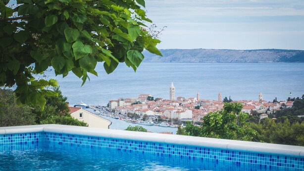 A swimming pool with a view of a coastal town and a mountain range in the background.