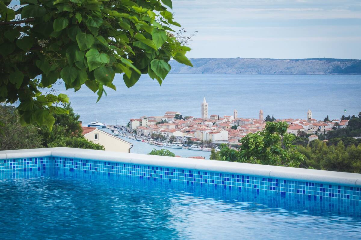 A swimming pool with a view of a coastal town and a mountain range in the background.