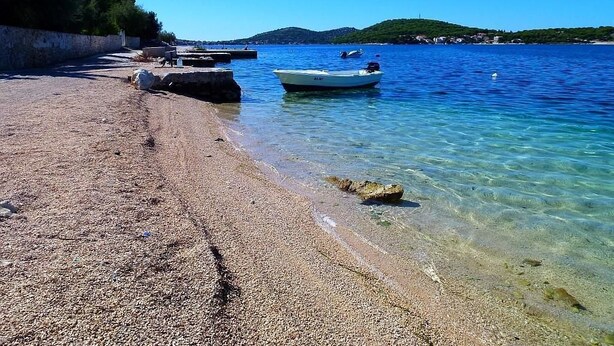 Une plage de galets, avec des bateaux et une mer d’un bleu limpide.