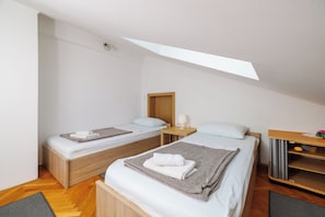 Una habitación pequeña y moderna con dos camas de madera, un escritorio y un tragaluz.
