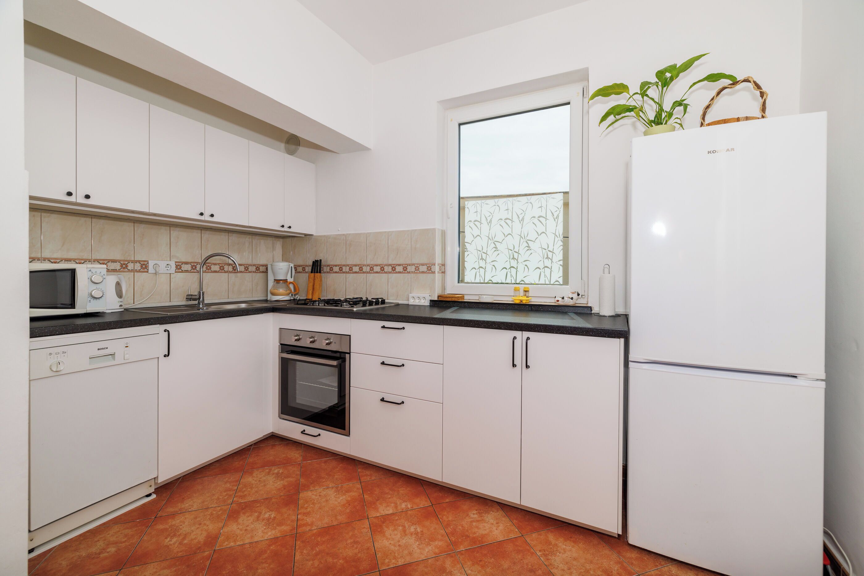 A kitchen with white cabinets, a stove, a microwave, and a refrigerator.