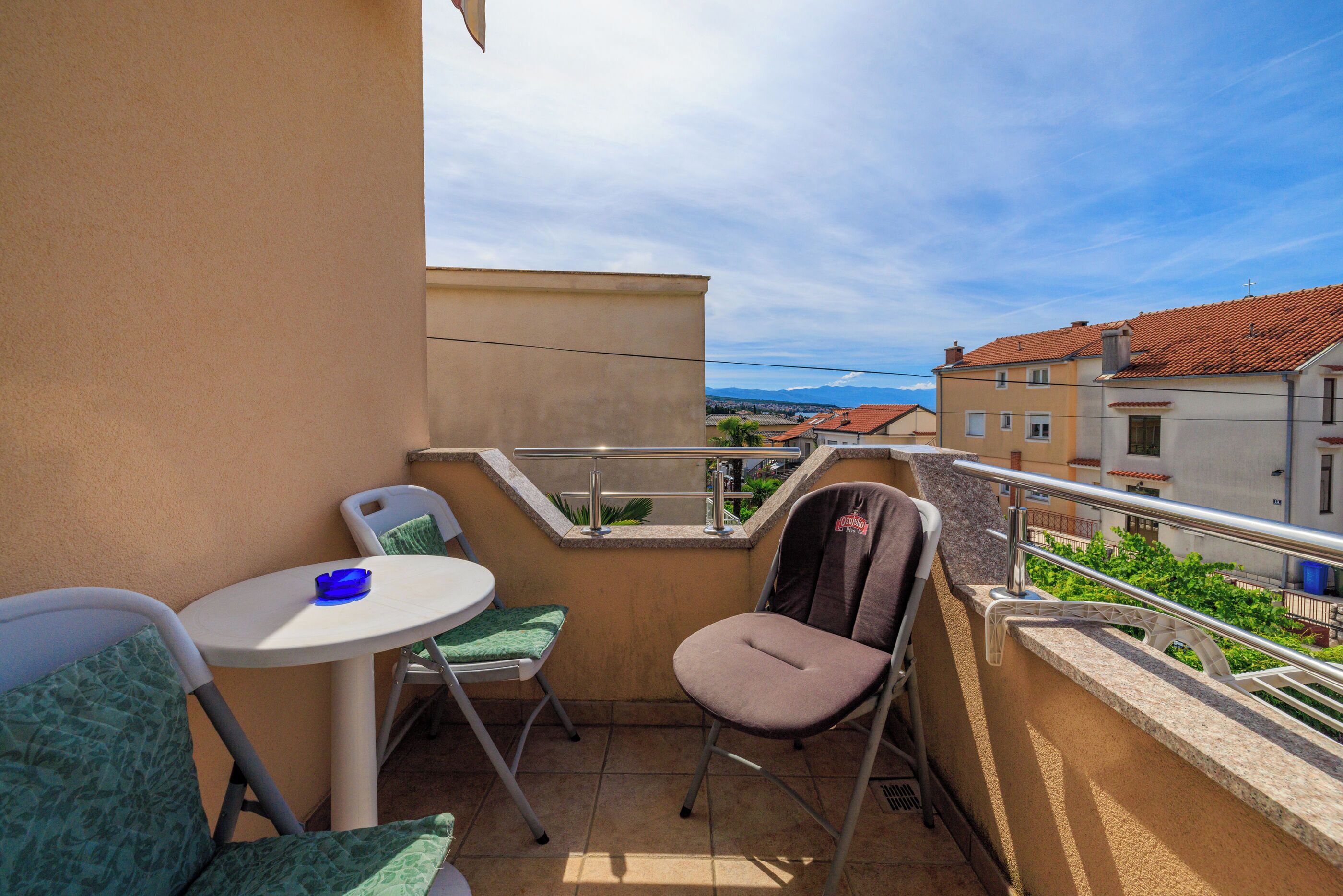 A balcony with a small table and two chairs, a metal chair, and a view of the cityscape.