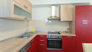 A modern kitchen with wooden cabinets, a stainless steel oven, and a red accent wall. - Apartments Konta (Kastela)