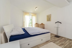 A bedroom with a bed, a bedside table, a floor lamp, and a window with curtains. - Apartments Konta (Kastela)