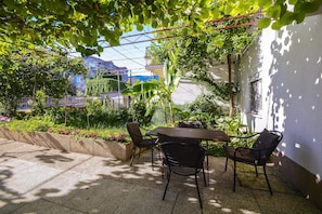 An outdoor patio with a table and chairs, surrounded by greenery and a white wall. - Apartments Konta (Kastela)