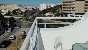 A view from a balcony overlooking a street with parked cars and buildings.