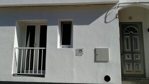 A building with a white facade, two windows with shutters, a small balcony, and a door with a decorative design.