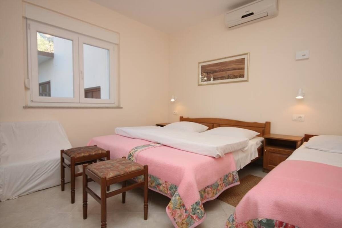 A bedroom with two beds, a chair, a bedside table, a window, and a wall-mounted picture.