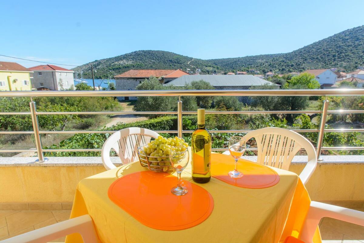 A balcony with a table set for two, featuring a bottle and a bowl of grapes.