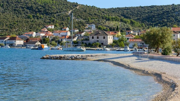 A coastal town with buildings along the waterfront, a pebbled beach, and boats docked near the shore. - Apartments Anton (Marina)